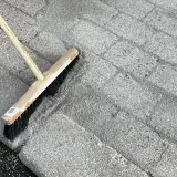 En kvast används för att ta bort mossa på stenplattor.