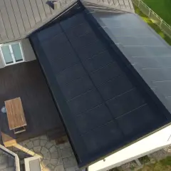 Tak med svensktillverkade solceller som täcker en stor del av takytan. Ett modernt hus med trädäck och grönskande trädgård.