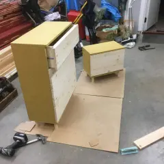 Pågående projekt att bygga byrå med lådor i trä och en gul topp. Verktyg som skruvdragare och hammare ligger bredvid.