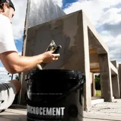 Man applicerar microcement utomhus på en betongkonstruktion. En hink med "Microcement" syns i förgrunden.
