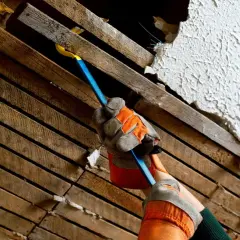 Hand med handske använder kofot för att ta bort innertakets träribbor och puts.
