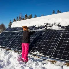 Person snöar av solceller i vinterlandskap.