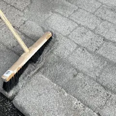 En kvast används för att ta bort mossa på stenplattor.