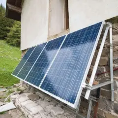 Solceller monterade på en stenvägg vid en grön sluttning. Solpanelerna fångar solljus för att driva huset.