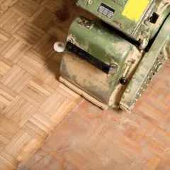 En golvslipmaskin står på en parkett av ek. Dammet visar att arbetet med att slipa ekparkett är i full gång.