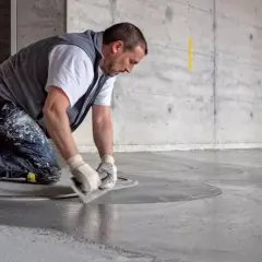 Man knäböjer och använder en bredspackel för att flytspackla ett betonggolv.