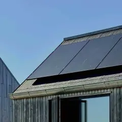 Tak med monokristallina solceller och träfasad mot blå himmel.