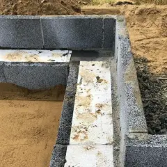Grundläggande arbete med lecablock. En del av grunden är färdigbyggd med grå lecablock och isolering. Sand och jord syns runt omkring.