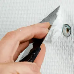Hand spacklar ett hål i en vit, strukturerad vägg med en spackel.
