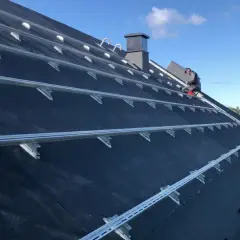 Montering av solceller på ett papptak. En person arbetar på taket, omgivet av byggställningar.