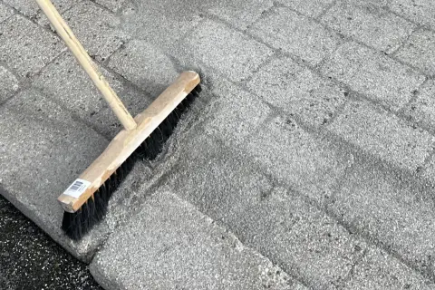 En kvast används för att ta bort mossa på stenplattor.