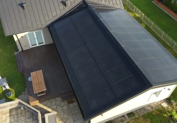 Tak med svensktillverkade solceller som täcker en stor del av takytan. Ett modernt hus med trädäck och grönskande trädgård.