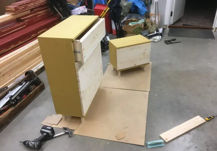 Pågående projekt att bygga byrå med lådor i trä och en gul topp. Verktyg som skruvdragare och hammare ligger bredvid.