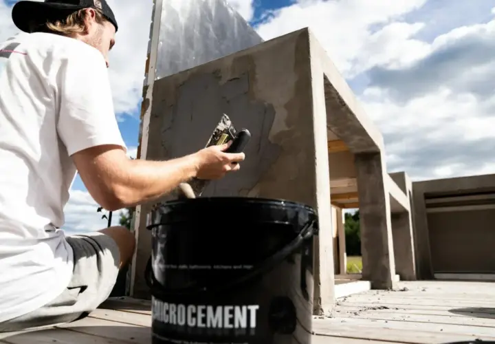 Man applicerar microcement utomhus på en betongkonstruktion. En hink med "Microcement" syns i förgrunden.