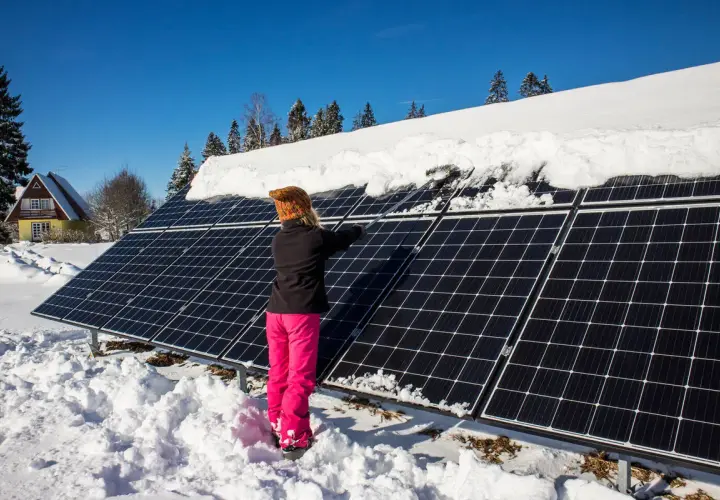 Person snöar av solceller i vinterlandskap.