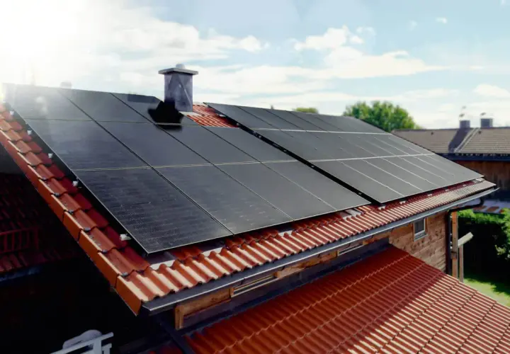 Solceller monterade på ett tegeltak. Solen skiner och fångas upp av panelerna.