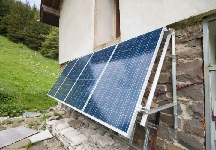 Solceller monterade på en stenvägg vid en grön sluttning. Solpanelerna fångar solljus för att driva huset.