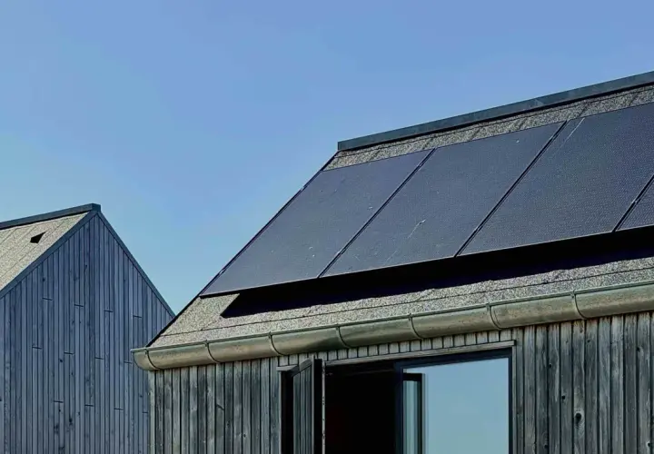 Tak med monokristallina solceller och träfasad mot blå himmel.