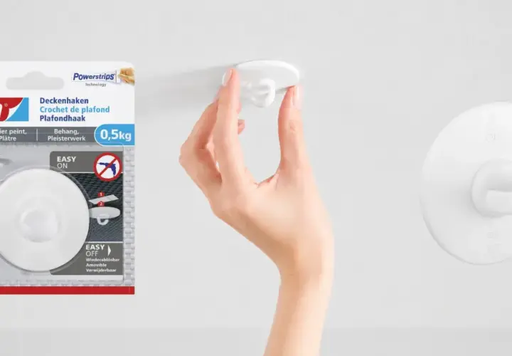 En hand fäster en vit krok i taket. Tesa Powerstrips-krok för tak, enkel att sätta upp och ta ner.