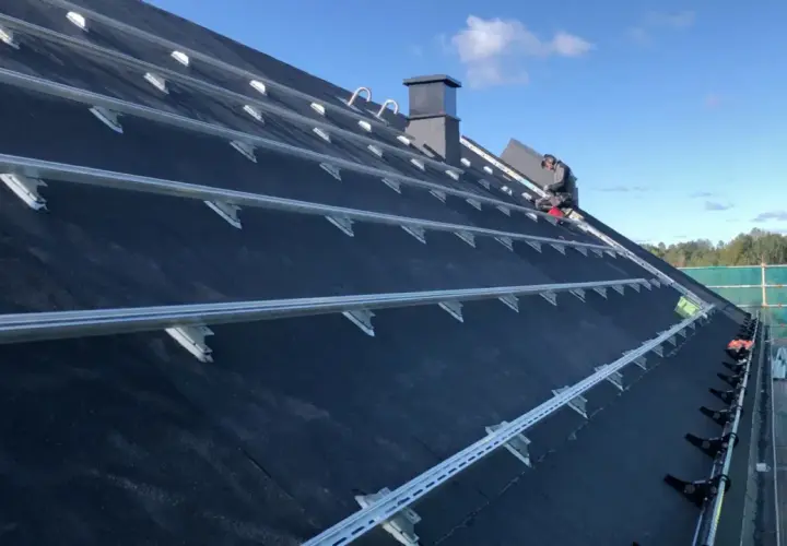 Montering av solceller på ett papptak. En person arbetar på taket, omgivet av byggställningar.