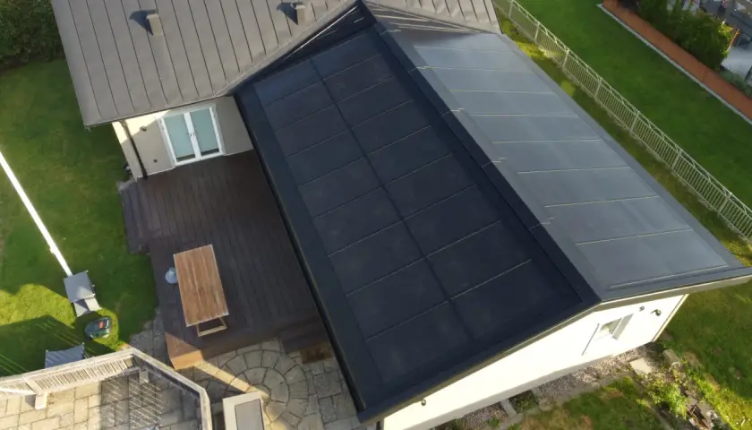 Tak med svensktillverkade solceller som täcker en stor del av takytan. Ett modernt hus med trädäck och grönskande trädgård.
