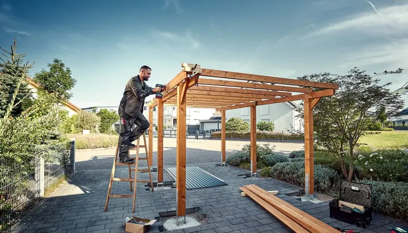 Man bygger carport med trästomme och skruvdragare.