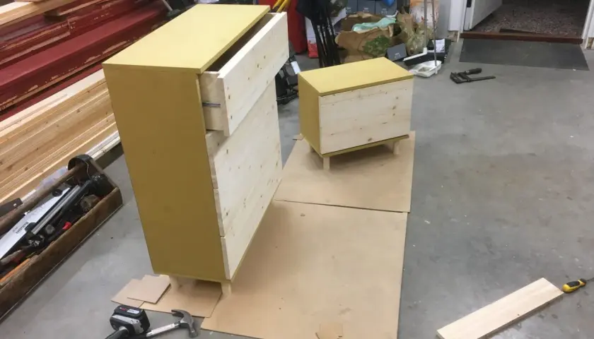 Pågående projekt att bygga byrå med lådor i trä och en gul topp. Verktyg som skruvdragare och hammare ligger bredvid.