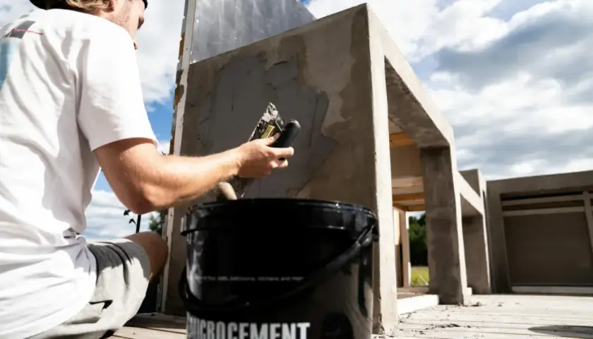 Man applicerar microcement utomhus på en betongkonstruktion. En hink med "Microcement" syns i förgrunden.
