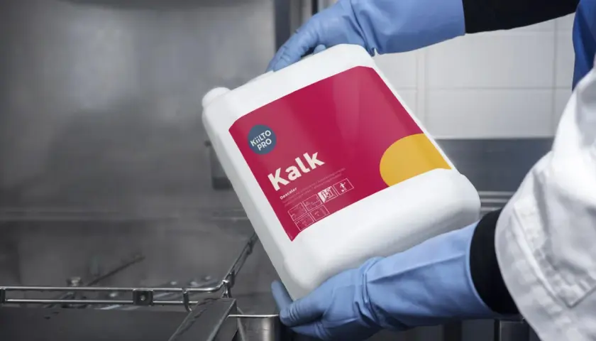 Hjälpmedel för att avkalka diskmaskin. En person i blå handskar håller en vit behållare med texten "Kalk" och "Descale".