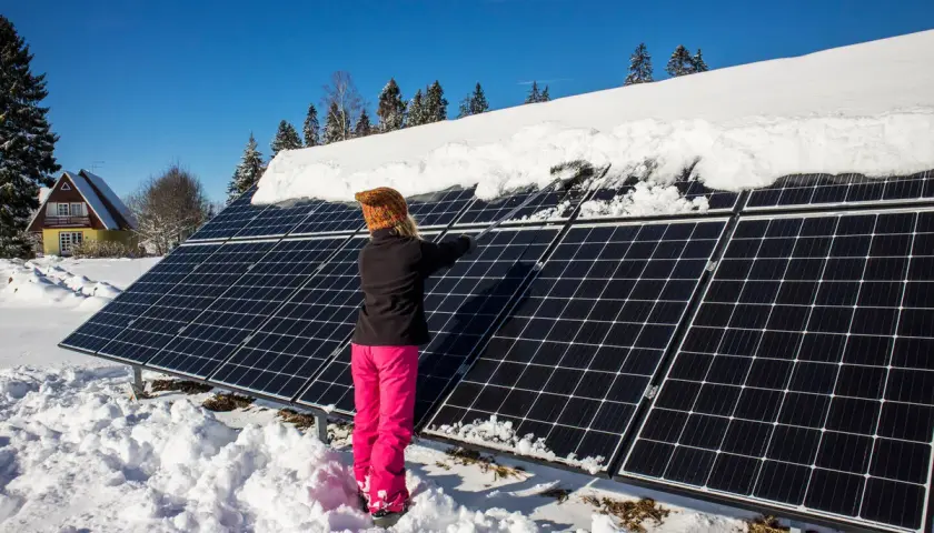 Person snöar av solceller i vinterlandskap.