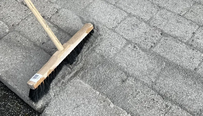 En kvast används för att ta bort mossa på stenplattor.