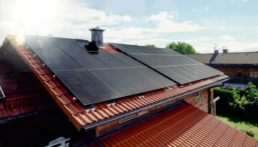 Solceller monterade på ett tegeltak. Solen skiner och fångas upp av panelerna.