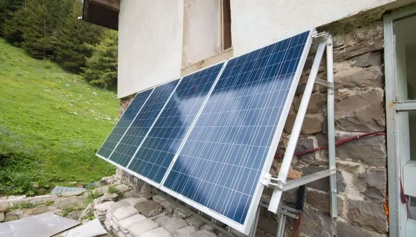 Solceller monterade på en stenvägg vid en grön sluttning. Solpanelerna fångar solljus för att driva huset.