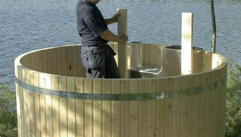 Man bygger badtunna vid en sjö. Träet är ljust och en metallring håller ihop tunnan.