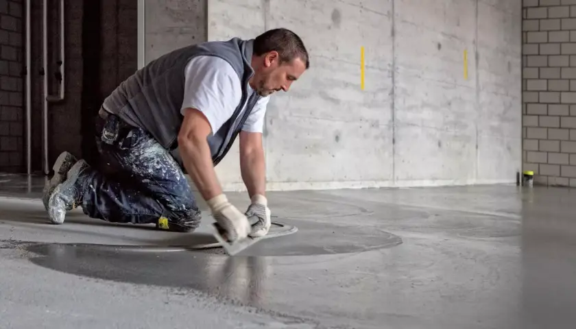 Man knäböjer och använder en bredspackel för att flytspackla ett betonggolv.