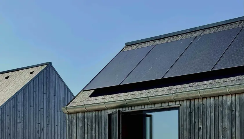Tak med monokristallina solceller och träfasad mot blå himmel.