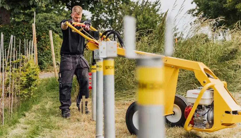 Man använder en markskruv-maskin från Biltema för att sätta stolpar i marken.