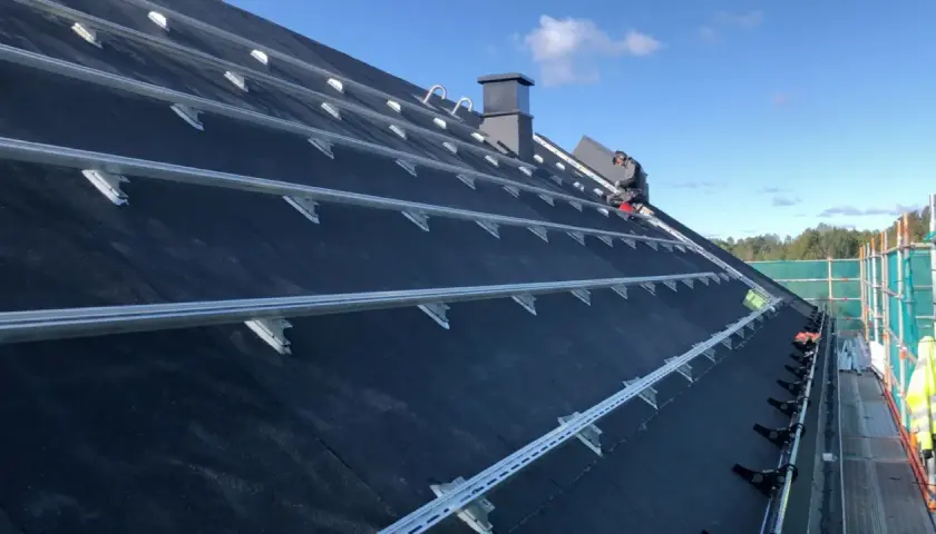 Montering av solceller på ett papptak. En person arbetar på taket, omgivet av byggställningar.