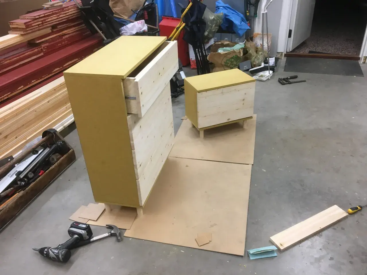 Pågående projekt att bygga byrå med lådor i trä och en gul topp. Verktyg som skruvdragare och hammare ligger bredvid.