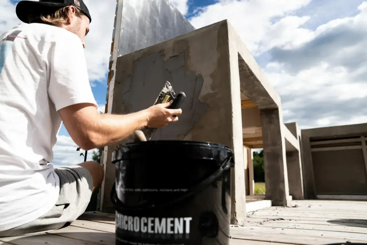 Man applicerar microcement utomhus på en betongkonstruktion. En hink med "Microcement" syns i förgrunden.