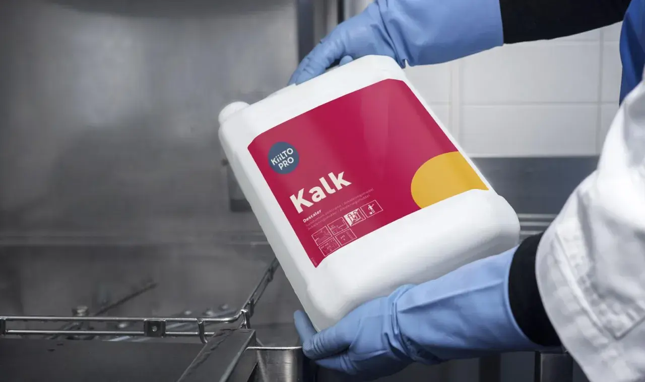 Hjälpmedel för att avkalka diskmaskin. En person i blå handskar håller en vit behållare med texten "Kalk" och "Descale".