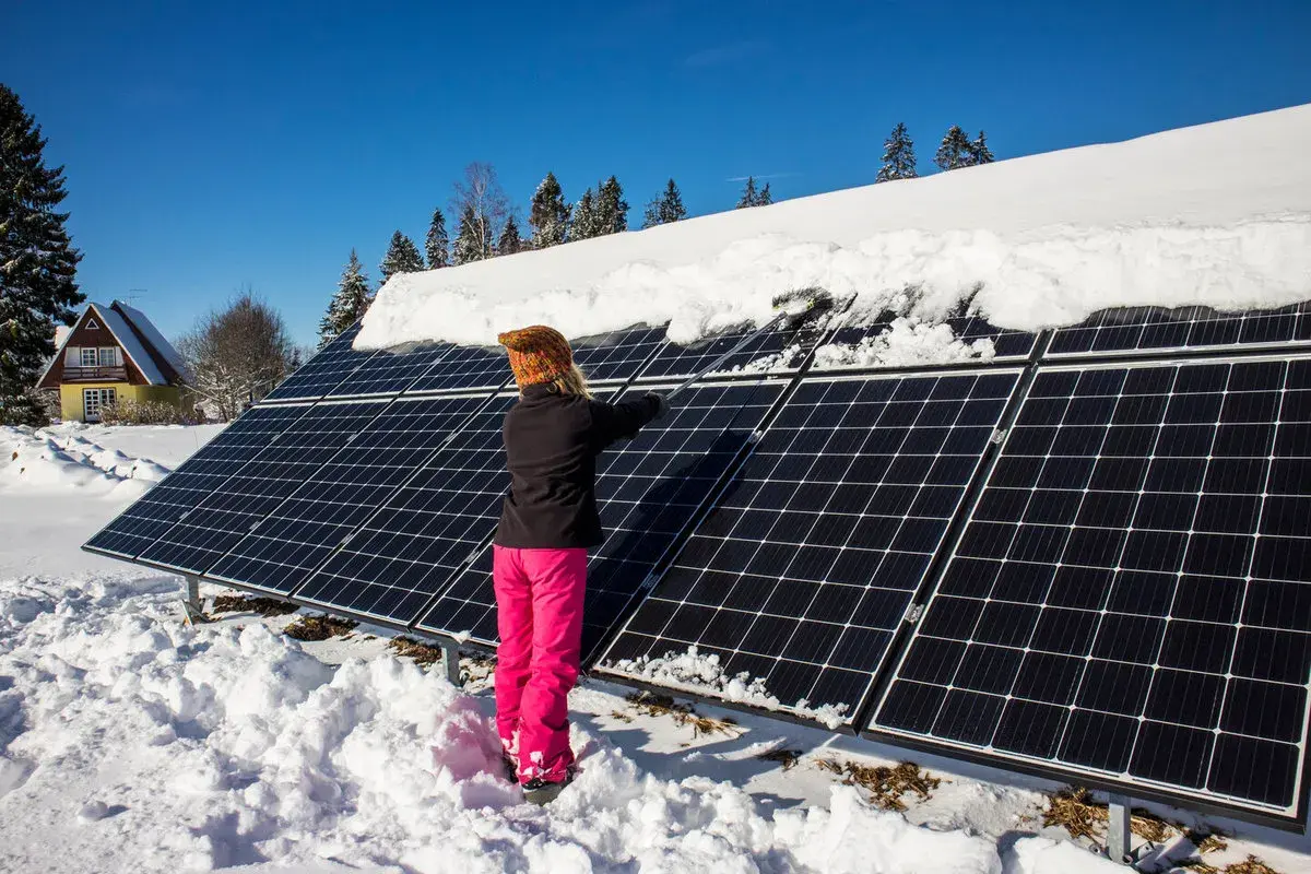 Person snöar av solceller i vinterlandskap.