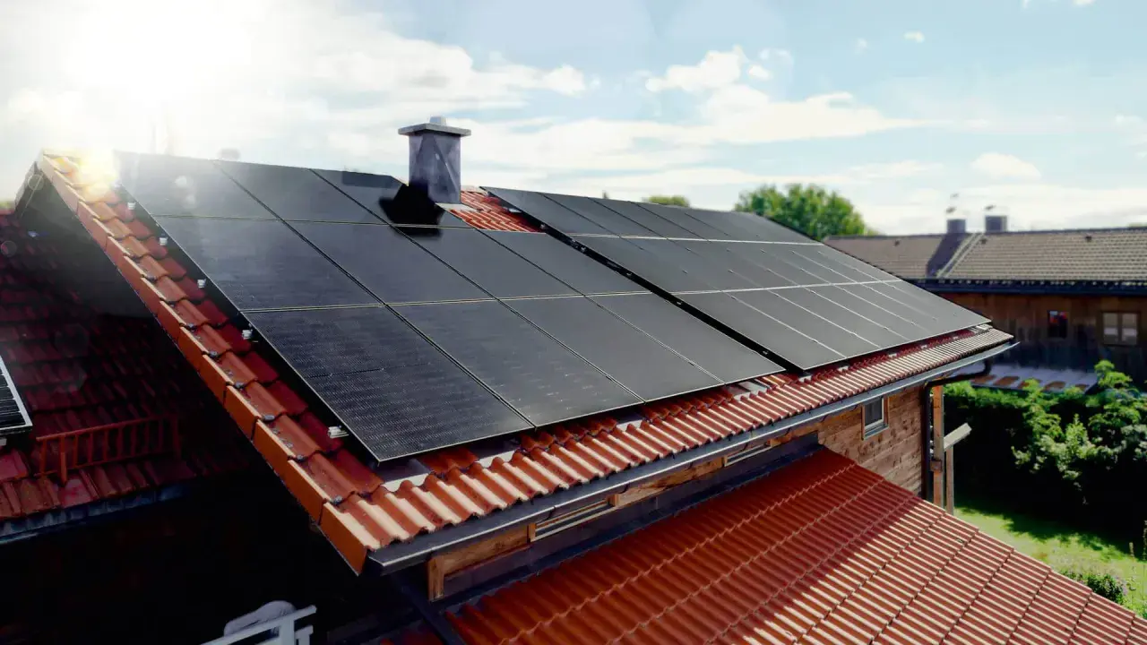 Solceller monterade på ett tegeltak. Solen skiner och fångas upp av panelerna.