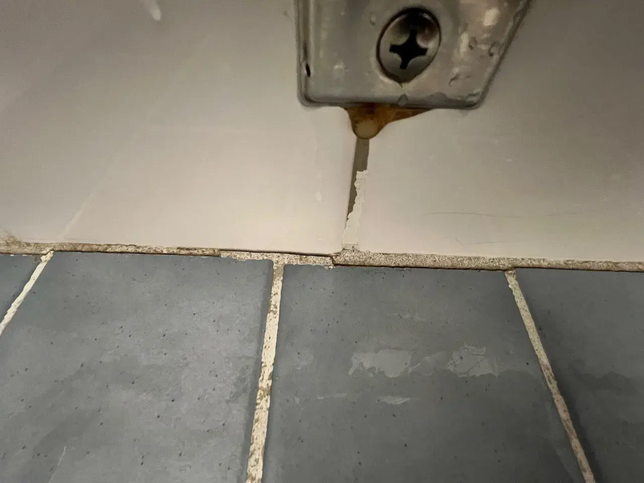 En misslyckad fogning kakel visar sprickor och smuts vid en skruv.