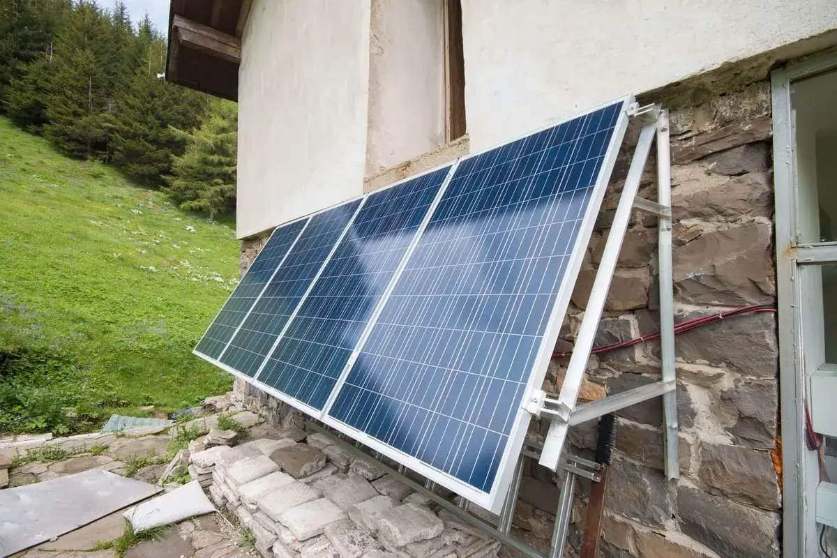 Solceller monterade på en stenvägg vid en grön sluttning. Solpanelerna fångar solljus för att driva huset.