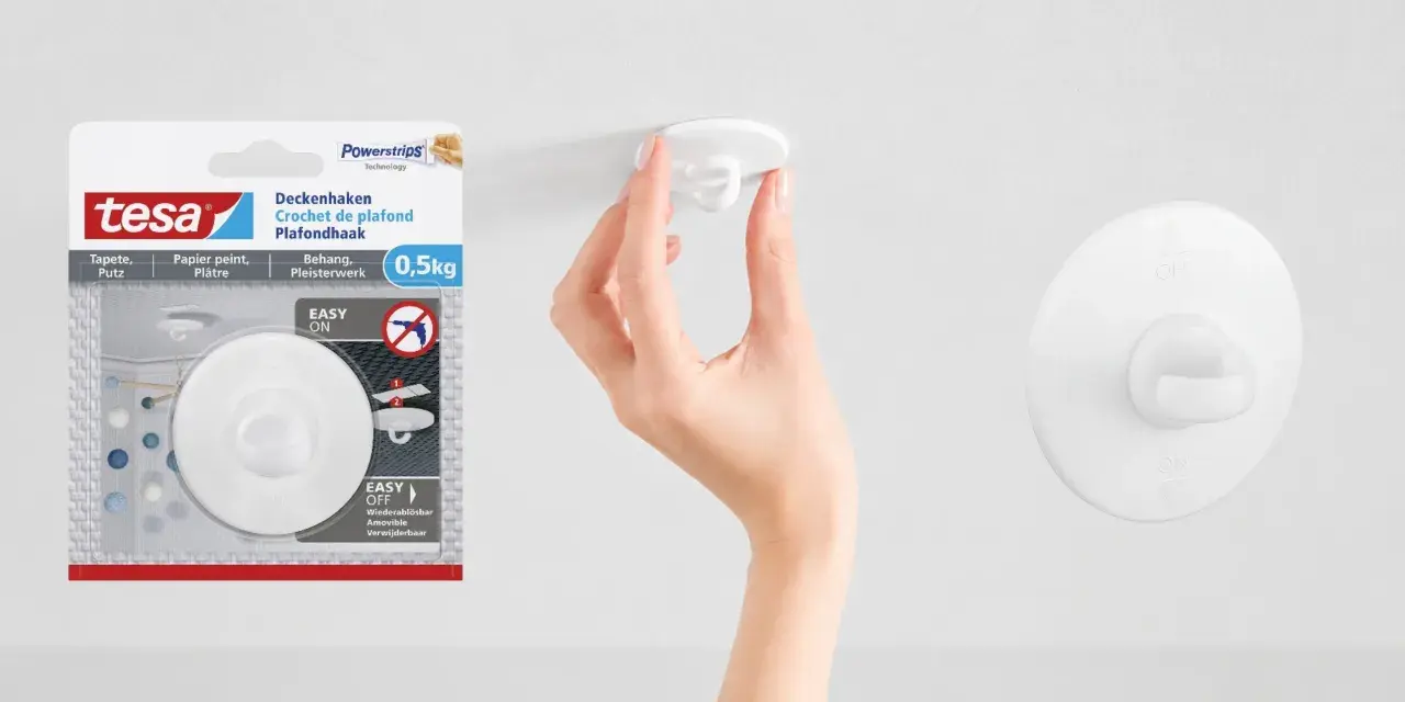 En hand fäster en vit krok i taket. Tesa Powerstrips-krok för tak, enkel att sätta upp och ta ner.