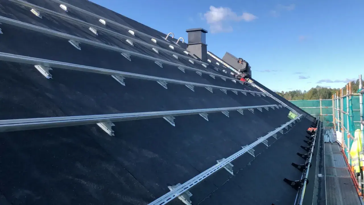 Montering av solceller på ett papptak. En person arbetar på taket, omgivet av byggställningar.
