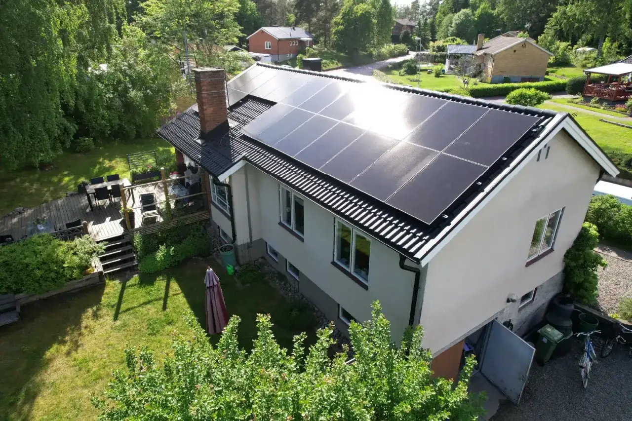 Tak med solceller installerade. Ett hus i en lummig trädgård med altan och utemöbler.