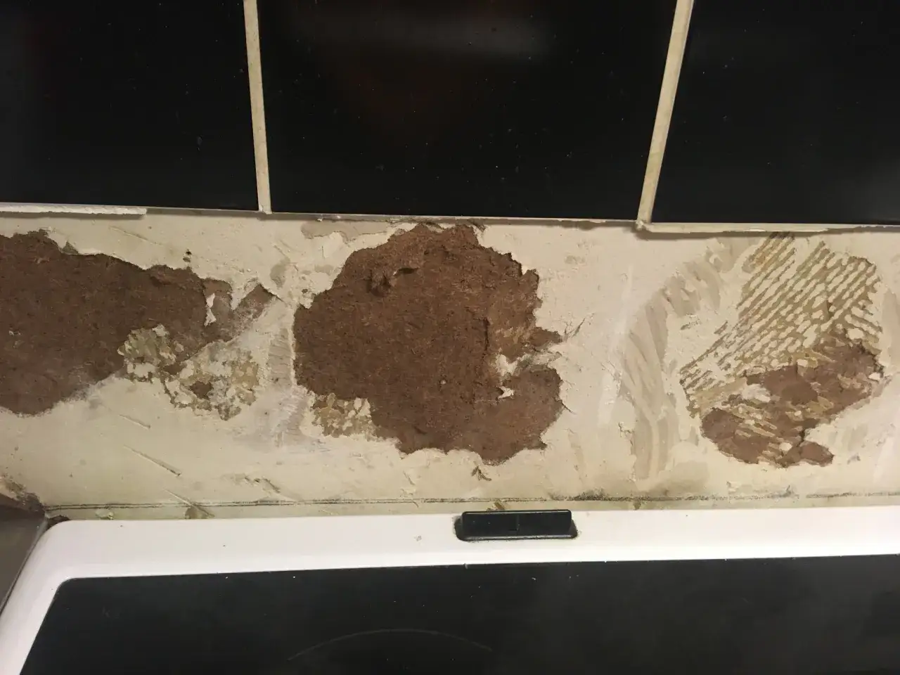 Skadad v&auml;gg under svart kakel, d&auml;r puts lossnat och exponerar tr&auml;fiberskiva. Dags att putsa p&aring; kakel igen.