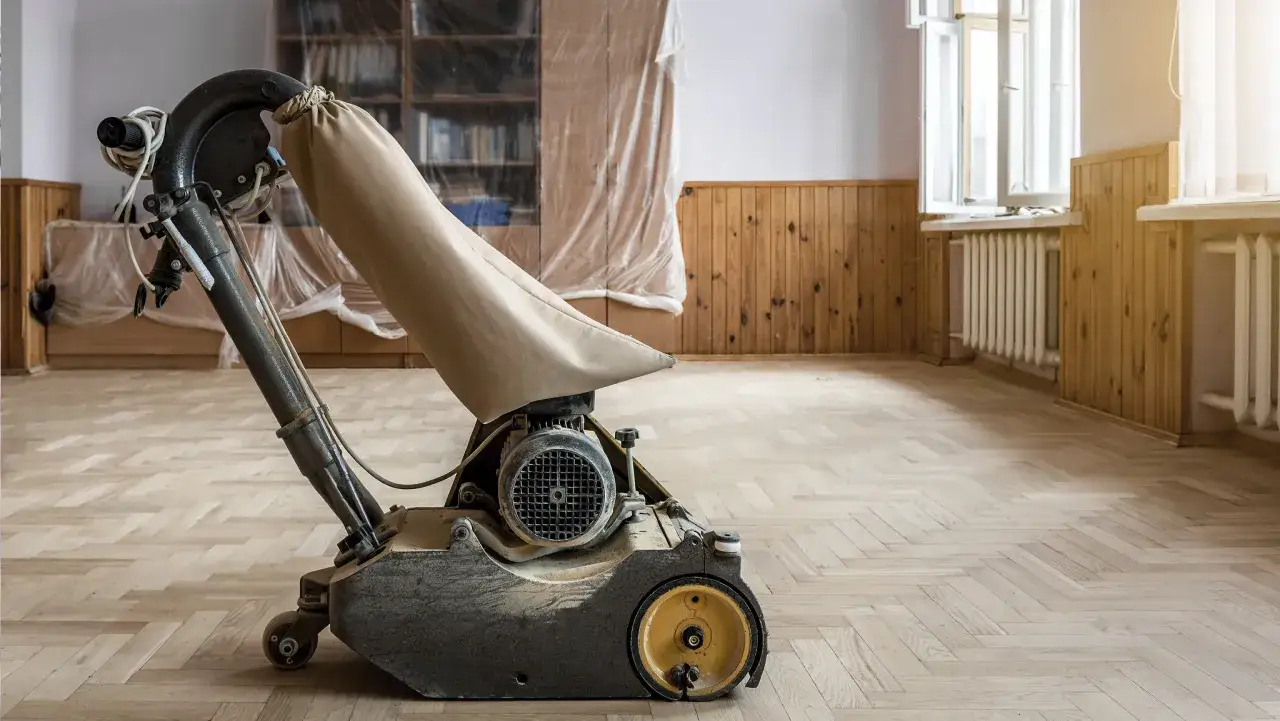 Golvslipmaskin redo att slipa parkettgolv i ett rum under renovering.